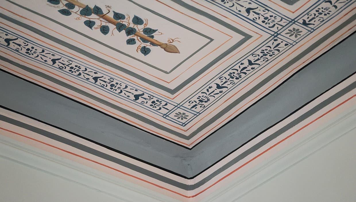 A corner of a hand-painted ceiling and its stencilled border
