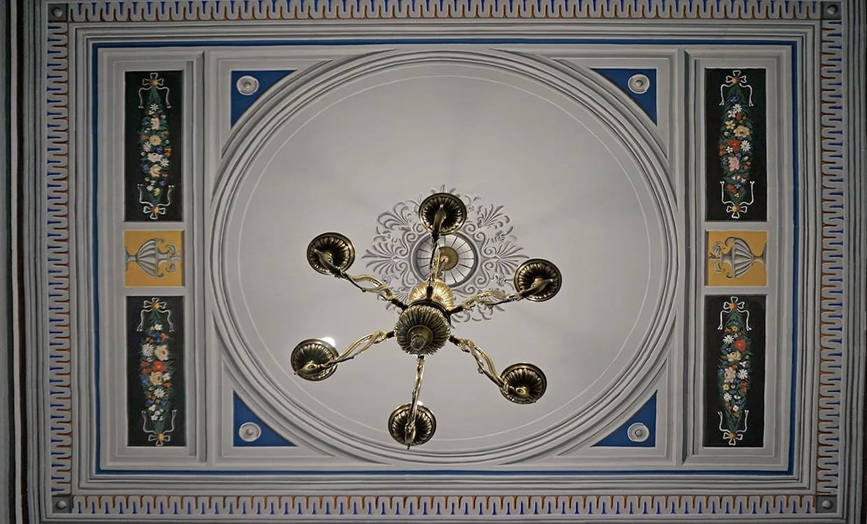 A restored painted ceiling with its floral panels and brass chandelier