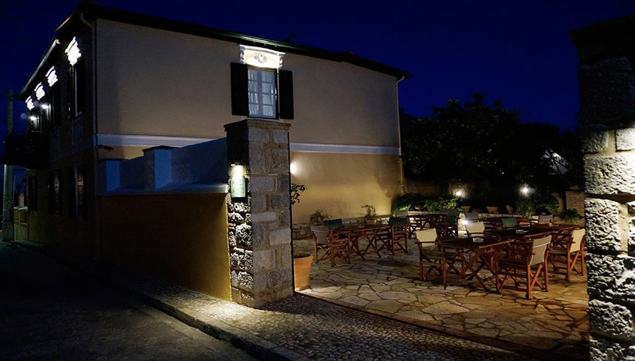 Nostos Hotel lit up at night, seen from the cobbled lane outside